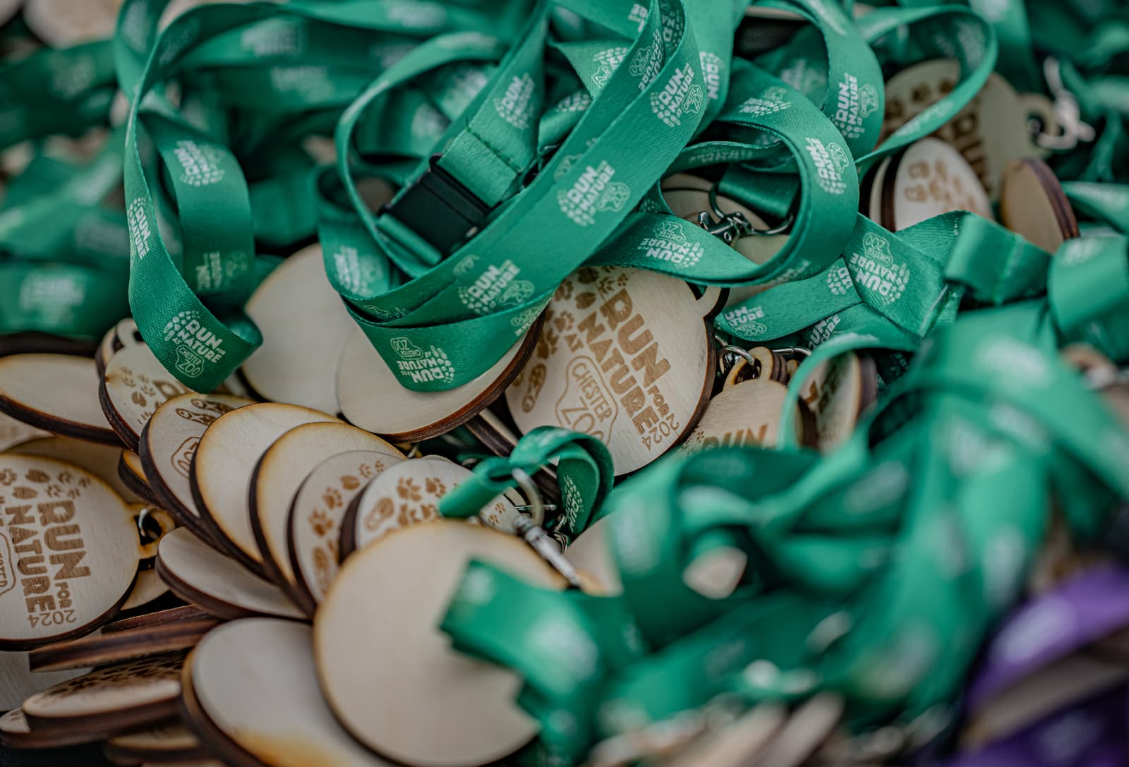 A pile of wooden medals with green ribbons that read “Run for Nature 2024.” The medals are stacked together, and the text is visible on several ribbons and on the wooden surfaces.