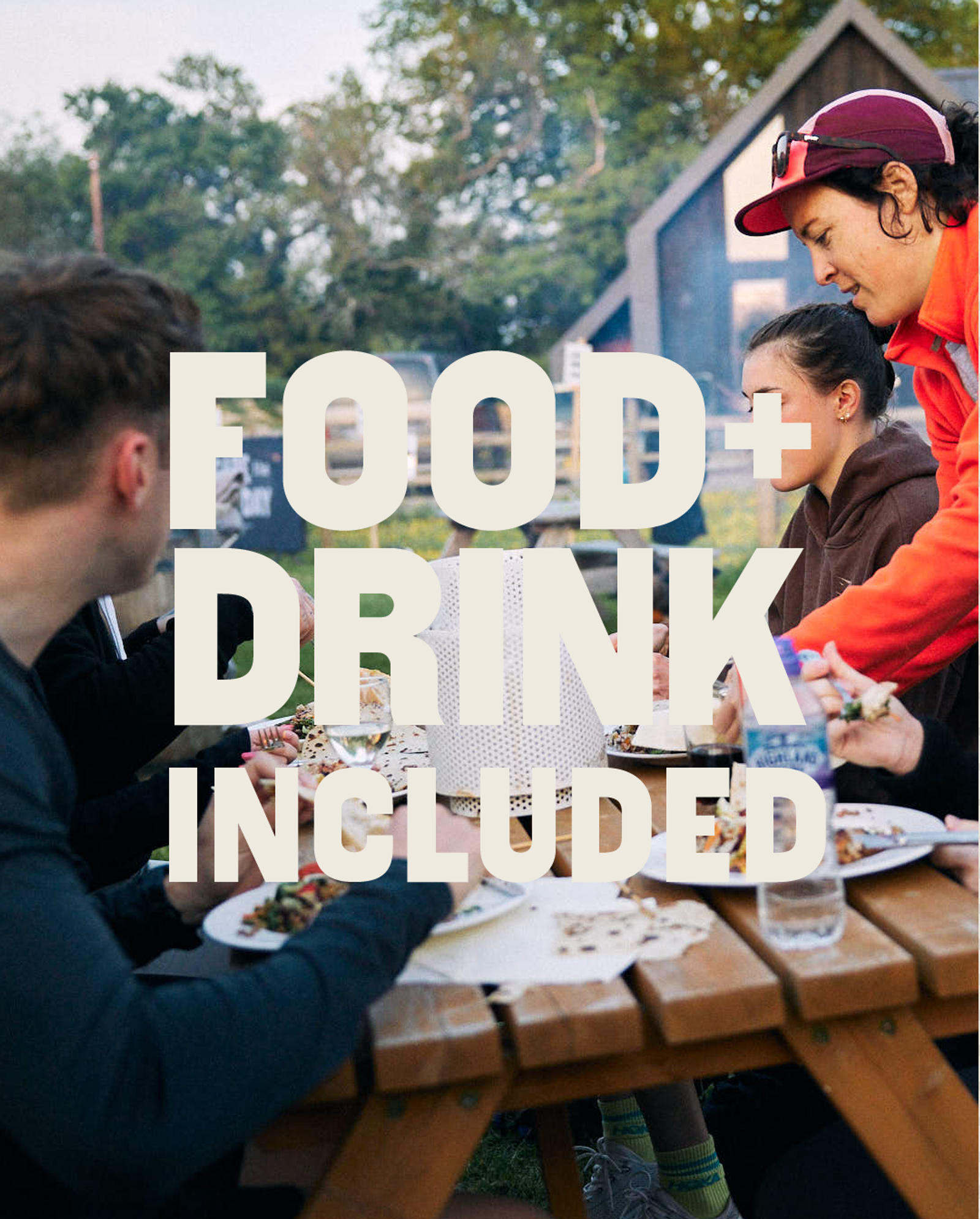 Four people sit at a wooden picnic table outdoors, sharing a meal. Plates of food and drinks are on the table. Large text over the image reads, “FOOD + DRINK INCLUDED.” Trees and a building are visible in the background.