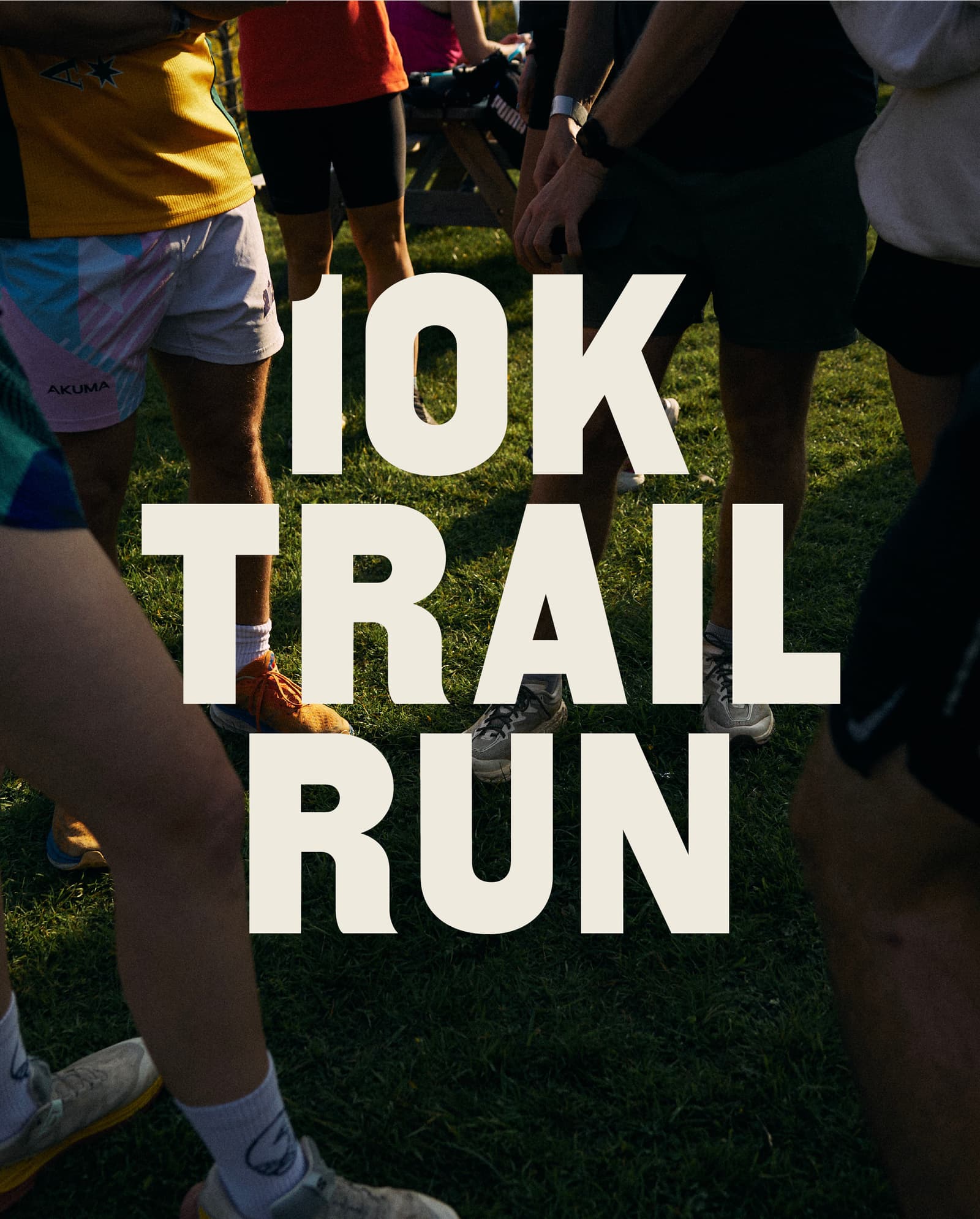 A group of runners standing together on grass, their legs visible, with large white text overlaid reading "10K TRAIL RUN.