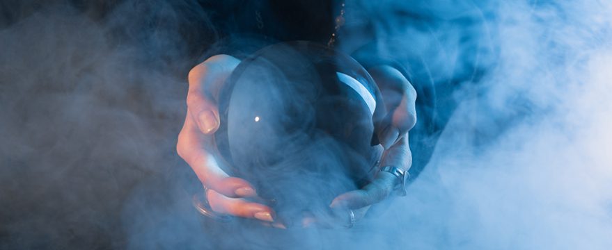 A person holding a crystal ball in both hands, surrounded by swirling blue and white smoke, creating a mysterious and mystical atmosphere.