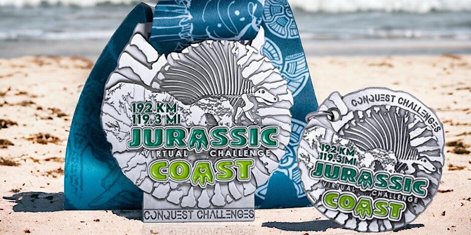 Two Jurassic Coast Virtual Challenge medals with a dinosaur and fossil design sit on sand, accompanied by a blue lanyard with fish illustrations. The medals display the distances "192.7 KM | 119.3 MI".