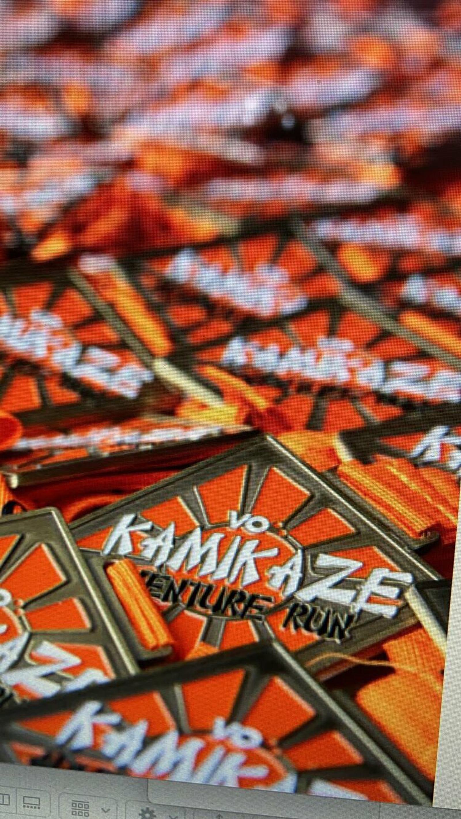 A pile of medals with orange and black designs, featuring the text "Kamikaze Adventure Run." The medals have a starburst pattern in the background and are displayed in a stack, suggesting they are awards for an adventure run event.