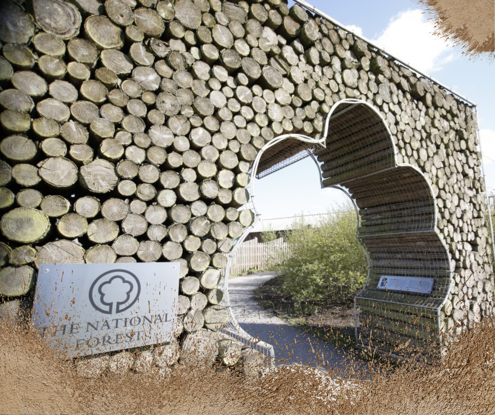 Entrance gate made of stacked logs at The National Forest. A sign with a tree logo and "The National Forest" text is on the left. The path leads through a uniquely shaped archway, showcasing natural elements and a bright, clear sky overhead.