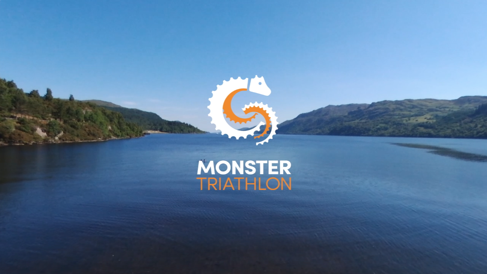 A serene lake under a clear blue sky with forested hills on either side. In the center foreground, a stylized seahorse logo with the text "Monster Triathlon" is overlaid.