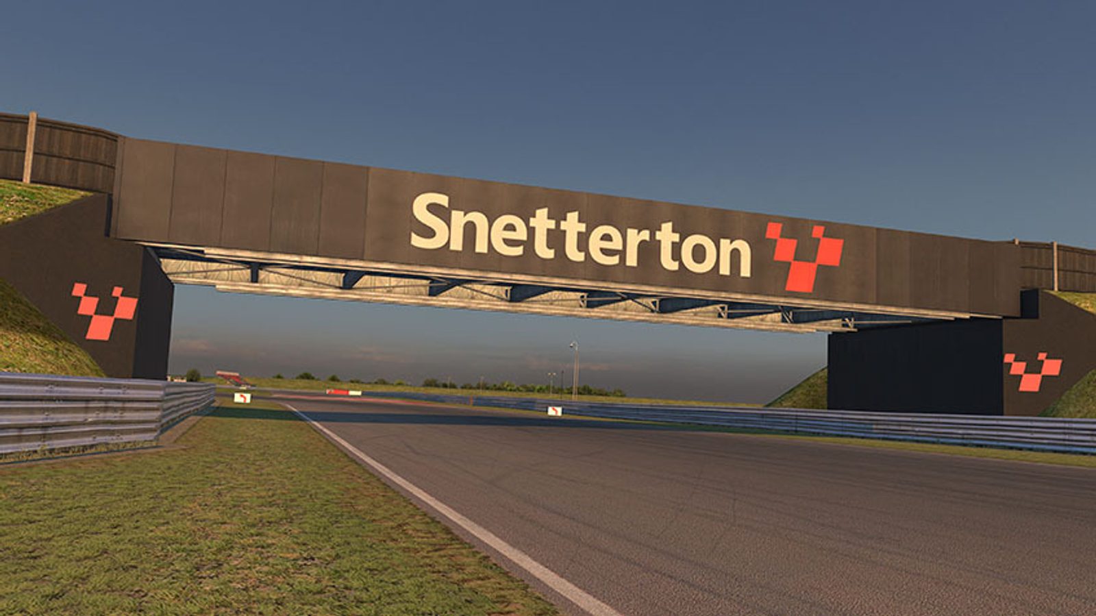 A view of the Snetterton race circuit, showing a track under a bridge with "Snetterton" and a red checkered flag logo displayed on the bridge. The track is surrounded by grass with a clear sky in the background.